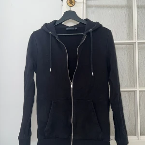 Svart hoodie från ASOS DESIGN - Säljer en svart hoodie från ASOS DESIGN i storlek S. Den har en dragkedja framtill, två fickor och en justerbar huva med dragsko. Perfekt för en avslappnad och bekväm stil. Använd men i bra skick.