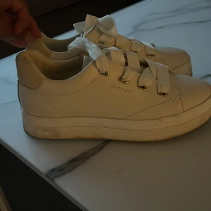Vita sneakers från Gant - Ett par vita sneakers från Gant med snörning och en tjock sula. Skorna har en enkel och stilren design med Gant-logotypen på sidan och baksidan.