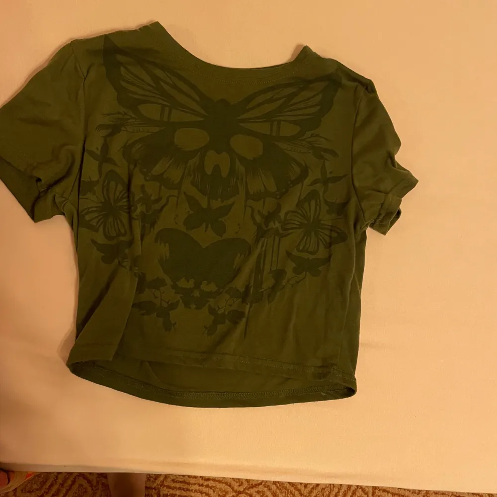 En grön tröja med korta ärmar och ett stort fjärilsmönster på baksidan. T-shirten är tillverkad i bomull. Skriv gärna om ni har frågor 💕💕. T-paidat.