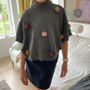 Grå stickad tröja från Hust and Claire - En grå stickad tröja från Hust and Claire med färgglada bollar i rött, rosa och gult. Tröjan har en polokrage och är perfekt på både en tunn och tjock tröja under med ribbstickade muddar vid nederkant.