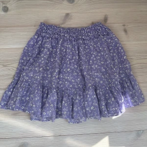 Lila kjol - Jag säljer en super fin lila kjol med ett vitt blomm-mönster. Kjolen är från zara i storlek S. Den är i nyskick och perfekt om man ska utomlands nu i vinter💕