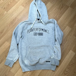 Peak performance hoodie - Grå färg med blåvit logga över bröst. Storlek small. 