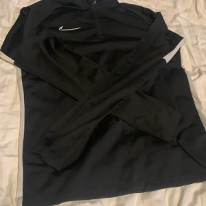 Nike träningströja (barnstorlek XL) - Enkel och snygg träningströja i bekvämt material med dragkedja vid halsen. Bra skick. Sitter som en Medium i damstorlek och S i herrstorlek.