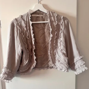 Bolero - söt bolero med fina volang detaljer . Är i en beige/lila färg 💜💜 saknar ett av knäppena för att kunna knäppa koftan .