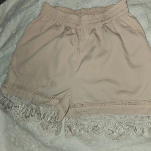 Puderrosa shorts med spetsdetaljer - Ett par puderrosa shorts med elastisk midja och spetsdetaljer vid fållen. Shortsen har en lös passform och är dekorerade med broderade mönster längs nederkanten. tyvärr kom inte rätta färgen fram på bilderna.  nypris 279