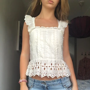 Vit topp från Zara - En vit topp från Zara med spetsdetaljer och volanger. Toppen har en elasisk rygg av smock för bättre passform. Den är dekorerad med brodering och har en volangkant längst ner. Det är storlek 164 men jag skulle säga att det är XS.