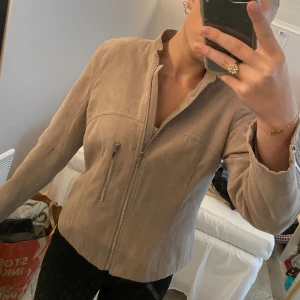 Beige täckjacka med silvriga detaljer  - Jag säljer min supersnygga täckjacka. Den har en silrig dragkedja. Den kommer från märket Jensen och är i storlek 38. Utmärkt skick.