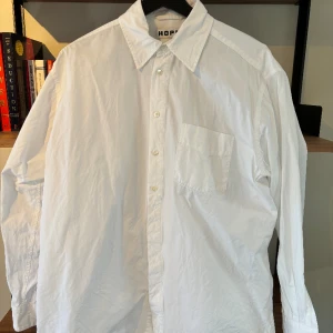 Hope Skjorta - Vit skjorta från Hope med en fick vid bröstet, passformen är oversized och ser lika fin ut på tjejer som på killar