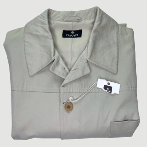 SAND - Skjortjacka - Storlek L - VARAN KAN KÖPAS DIREKT PÅ VÅR HEMSIDA, ettmarke.se MÄRKE: SAND. FÄRG: Ljusbeige. MODELL: Klassisk skjortjacka med fodring. STORLEK: L. AXELBREDD (SÖM TILL SÖM RAKT ÖVER): 53 cm. TOTALLÄNGD (FRÅN KRAGEN): 82 cm. BREDD NEDTILL (PLATT MÅTT): 60 cm. 