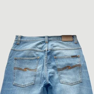 Nudie Jeans - Raka Jeans - Storlek 31 - VARAN KAN KÖPAS DIREKT PÅ VÅR HEMSIDA, ettmarke.se MÄRKE: Nudie Jeans. MODELL: Thin Finn. FÄRG: Ljusblå. STORLEK: W31 L32 enligt lapp. MIDJA RAKT ÖVER: 40,5 cm. MIDJEHÖJD: 25 cm. TOTALLÄNGD (FRÅN MIDJAN): 109 cm. BENLÄNGD (FRÅN INNELÅRET): 84 cm