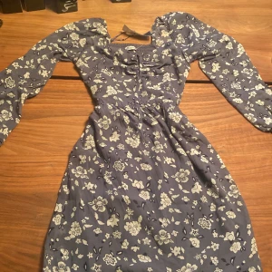 Hollister klänning - Jättefin grå-blå minidress med blommor från hollister. Aldrig använt den för att den tyvärr är för liten. Skriv om ni har några frågor. 