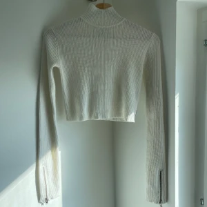 Långärmad crop top från Unif  - Vit, stickad crop top med hög krage och dragkedjor på ärmarna. Knappt använd, fint skick! 