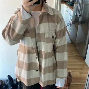 Beige jacka  - En fin skjortjacka som är rutig med skärp runt midjan. Det är en tunnare jacka för varma höstdagar. Jackan är i strl 36 (jag har vanligtvis 38) och ska vara lite oversized.
