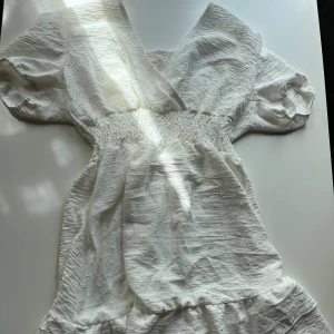 Vit sommarklänning storlek storlek s - En vit klänning med en v-ringning och korta ärmar. Klänningen har en elastisk midja och en volangad kjol. Endast provad.