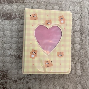 Gul och rosa plånbok med kattmönster - En söt binder med ett rutigt mönster i gult och rosa. binder  har små kattansikten som dekoration och ett hjärtformat fönster på framsidan. Den är kompakt och praktisk för daglig användning.