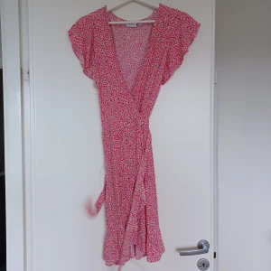 NY klänning  - En så snygg o romantisk klänning. Köptes förra året på Bubbleroom. Aldrig använd för har så många klänningar. Omlottklänning med liten volang på ärmen o nertill. Vit botten med ljus o mörkrosa blommor o lite grönt print. Viskos. Finns på Vinted också