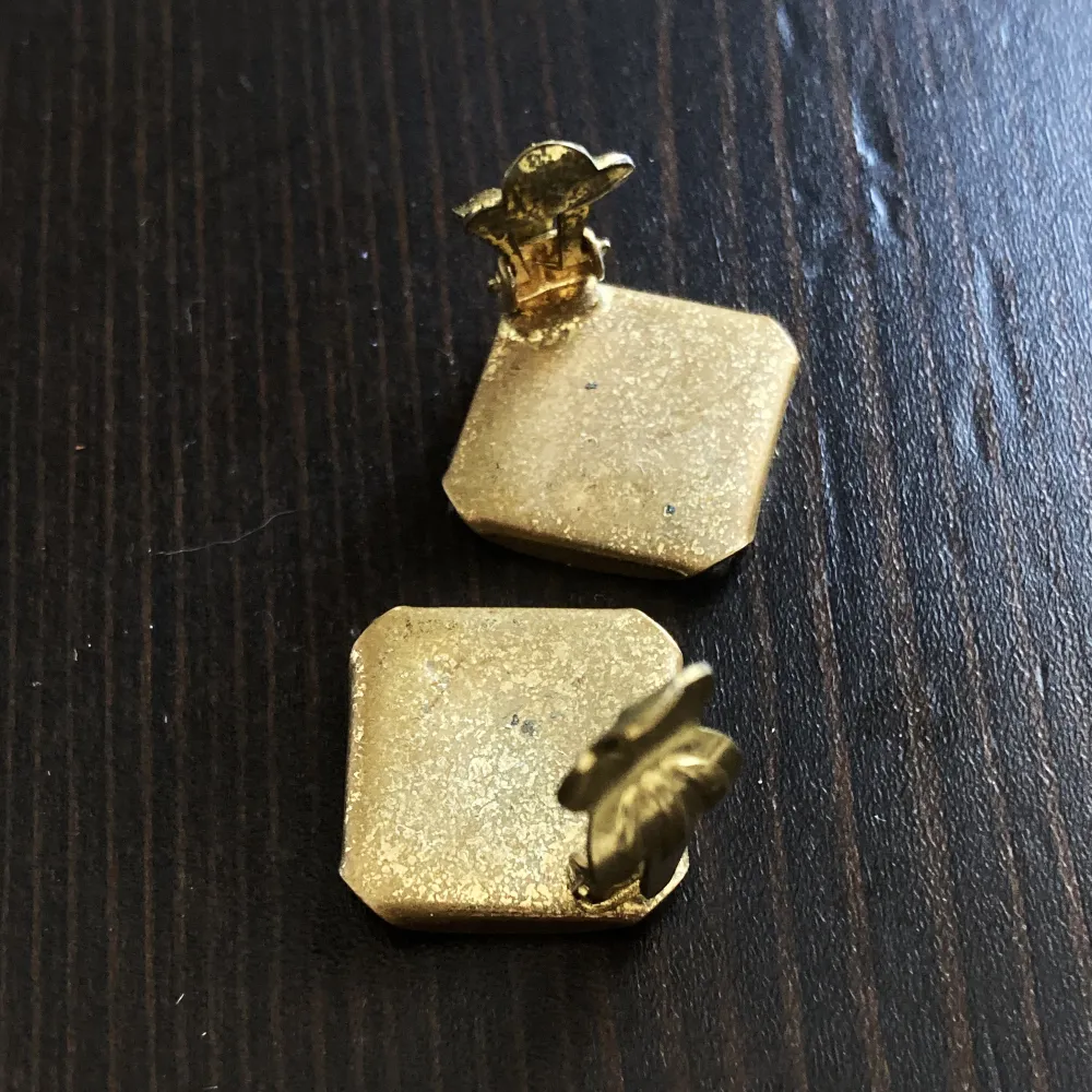 Clip-on örhängen i grönt & guldfärgad metall, finns missfärgningar och ena örhängets nypa är lite sned. Mått: 11x11 mm.. Accessoarer.