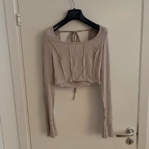 Crop-Top öppen rygg - En kort långärmad med utsvängda armar + slits och rosett bak. 