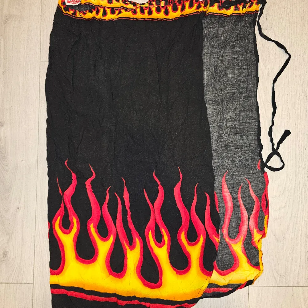 Beskrivning: Svart sarong med flames Märke: EMP Storlek: One size Skick: I mycket gott skick Material: 100% viskos  Nakenkatt finns i hemmet. Kjolar.