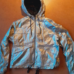 Silvrig Vindjacka - Cool jacka i silverfärgat material, storlek XS från H&M Divided. Passar även S. Lite boxy fit, ca 56 cm lång och 50 cm bred. I princip nyskick, använd väldigt lite.