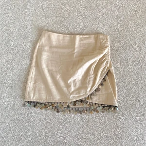 ZARA linnekjol med pärlor och ”snäckor” - Otroligt snygg kjol från ZARA i linne. Använd en gång. Saknas ett hänge men det syns inte vid användning. Någon ”snäcka” är också bruten.
