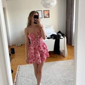Rosa/röd blommig klänning - Rosa/röd blommig klänning som är oanvänd. Man kan knyta banden vid halsen på olika sett (se första och andra bilden)