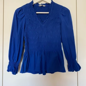 Blå blus  - Blå blus med resår i storlek S från Pigalle. Passar även som XS