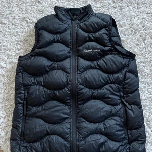 Peak Performance Väst - En svart väst från peak performance! I bra skick, dock ett litet hål på vänster sida bak (kolla bild) storlek 160 cm passar en XS i herrstorlek! 