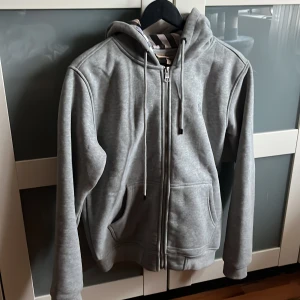 Burberry zip hoodie -  Säljer min brors Burberry hoodie som självklart är äkta. Han köpte den för 2 månader sen på NK och vill sälja den då den inte riktigt är hans stil. Skriv om ni har frågor såsom äkthetsbevis.!! Storlek M kan passa S. Vid snap affär kan pris diskutera