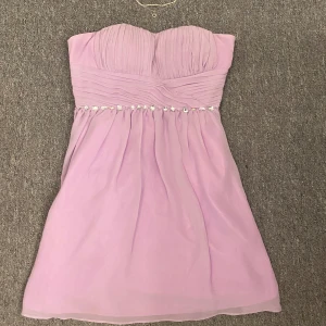 Ljuslila kortklänning - Ljuslila kortklänning med diamanter runt midjan. Det finns en liten dragkedja på ena sidan av klänningen. 