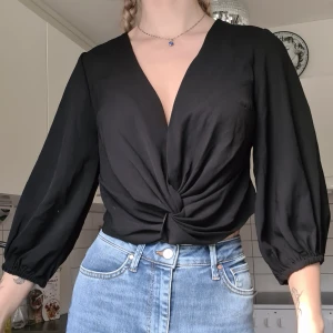 Svart blus  - Svart blus med trekvartsärm, v-ringad och snurrad framtill. Oanvänd, normal i storleken. Kom med prisförslag 😊  Material: 100% Polyester. 