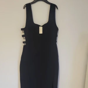 Svart elegant långklänning oanvänd  - Maxiklänning från NLY Eve Visa dina kurvor.  Öppet parti i sida med tre elastiska band Slits framtill Försluts med dragkedja samt hyska och hake baktill, fodrad. Bilderna gör den inte rättvisa kan skicka fler bilder om det önskas. Klänningen oanvänd