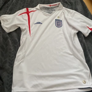 England Retro Tröja Barn Storlek 152cm riktig tror den är 2007/2008 - 9/10 skick jätte snygg och messa för mer bilder det finns massa små fina detaljer och den här går inte att köpa längre eftersom den är retro tröjan är riktig och säljer för 349kr men kan förhandlas England tröja säljer för att den inte passar längre 