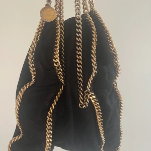 Stella McCartney falabella väska - Äkta jättefin stella mccarrney falabella väska.Svart med guldiga kedjor. Lite av den guldiga färgen har bleknat samma med lite av insidan men påverkar inte väskans användning. Använd men försiktigt och inga tydliga defekter. Äkthetskod finns i väskan
