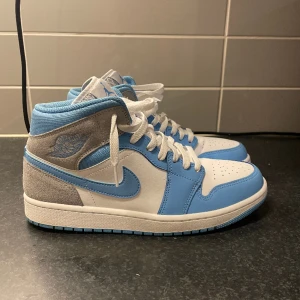 Jordan 1 Mid University Blue - Hej! Säljer dessa Jordans i super skick, köpta från merch sweden för 3000kr nya. Säljer dem pga de inte passar mig längre. Väldigt försiktigt använda det ända är att vänstra skon är lite lite creasad på högra sidan, skydd följer i. Strl 43   