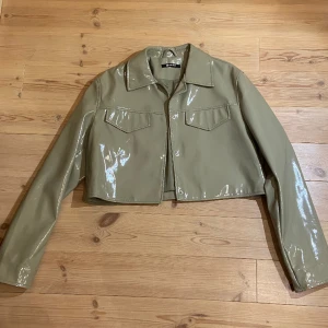 Olivgrön croppad lackjacka - Cool lackjacka i olivgrön färg från Gina tricot. Väldigt sparsamt använd så ser ut att vara helt ny. 