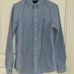 Ljusblå Ralph lauren skjorta med brun logga perfekt nu inför sommaren. Har bara användts ett par gånger. Nypris 1600.