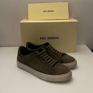 Mocka Axel Arigato - Snygga Axel Arigato skor i storlek 43. Skick 9/10 inga defekter förutom att guldiga färgen där det står Arigato vid sidan av skon är inte lika synlig Annars felfria och jag tvättar de innan de skickas Nypris 2400 Kom privat med frågor och prisförslag