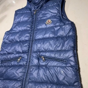 Moncler gui väst - Tjena! Säljer en moncler gui väst, i en sjukt snygg och ovanlig blå färg, västen är i toppskick, den är i storlek 14y i barn men passar xs i herr, perfekt inför våren, vid funderingar hör av er :)