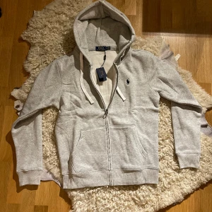 Polo Ralph Lauren Zip-Hoodie - Introducing a pristine gray Polo Ralph Lauren zip-up cardigan, impeccably maintained at a flawless 10/10 condition and still adorned with its original price tag. 