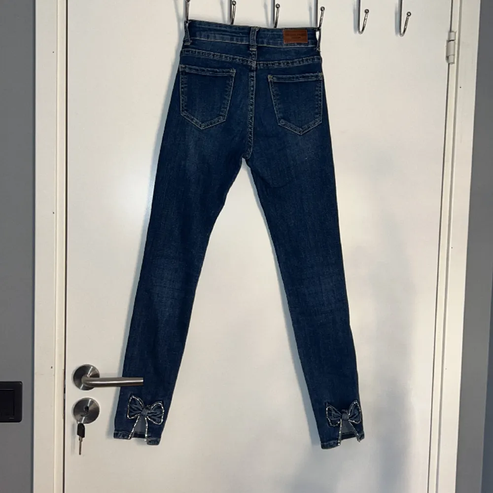 Ett par marinblåa skinni jeans från Redial Paris med rosetter på anklen. Storlek xs/34. (Väl använda). Rosetternas pärlband är lite av samt knappen på framsidan sitter lite löst med den går att laga. . Jeans & Byxor.
