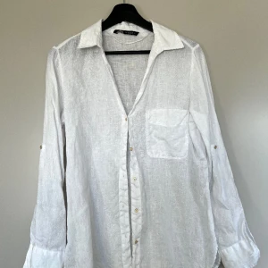 Linneskjorta ZARA - Vit skjorta i 100% linne från Zara. Gulddetaljer och möjlighet till att vika upp ärmarna med en liten knapp (se bild). Använd sparsamt så i fint skick. Storlek S 