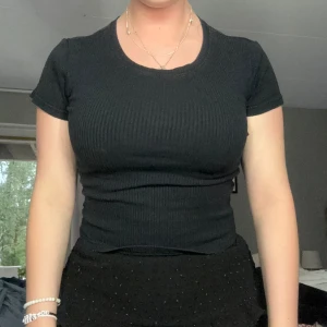 Svart tishirt - Detta är ett plagg som sitter tajt mot kroppen. Den ger dig en naturlig figur men samtidigt ett mjukt material mot huden. Plagget köptes för 179 jag säljer för 90kr. Det är ett plagg som man kan ha till vardags men ändå till en festligare ställning. 