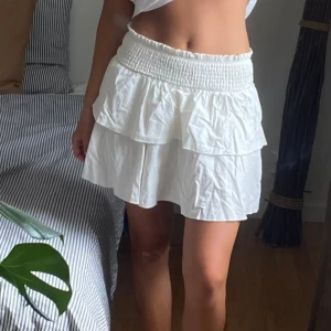 Vit volangkjol - Minikjol med volanger, små fläckar upptill, syns knappt och tror att set skulle gå bort i en tvätt. Köpt secondhand vet ej märke, skulle gissa att det är en S