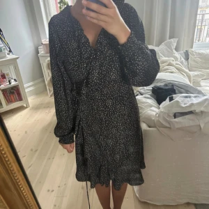 Prickig omlott klänning med volang  - Märkes klänning från JUST. Går omlott och kan därför passa många och är mkt justerbar. Har prickar på sig och volnag v-ringning samt muff vid armen