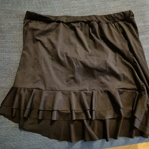 Svart badkjol - Oanvänd, men har blivit tvättad. Inbyggd trosa, resår i midjan, längre bak. Ca 90cm i midjan, ca 40cm lång fram, ca 50cm lång bak.
