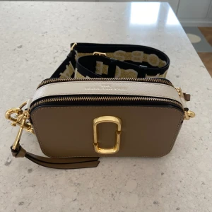 Marc Jacobs ”The Snapshot” Väska  - Säljer min Marc Jacobs ”The Snapshot” väska då den inte kommer till användning. Köptes sommaren 2021 men använd max 10 gånger. Lite skrapmärken på guldiga partierna men märks bara när man kollar nära alltså väldigt bra skick. Köpt för €330 på Irland.