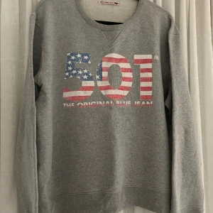 Vintage Levis crewneck - Sweatshirt från Levis, vintage. Grå tröja med tryck fram 501. Har en sydd lagning i sidan på tröjan, se foto. Snyggt lagad. I övrigt tvättblekt tryck men precis i rätt stuk. Material: Bomull 100 %