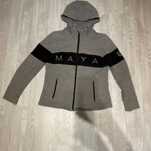 Grå hoodie - Säljer en grå och svart hoodie från maya Delorez. Tjockt och gosigt material. Sliten vid ärmarna men i övrigt väldigt fint skick. Storlek M, tänkte 350kr+frakt men jag är öppen för prisförslag 