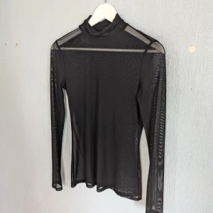 Svart mesh polotopp från Gina Tricot - En svart, genomskinlig mesh polotopp från Gina Tricot. Toppen har långa ärmar och en hög krage, vilket ger den en elegant och modern look.